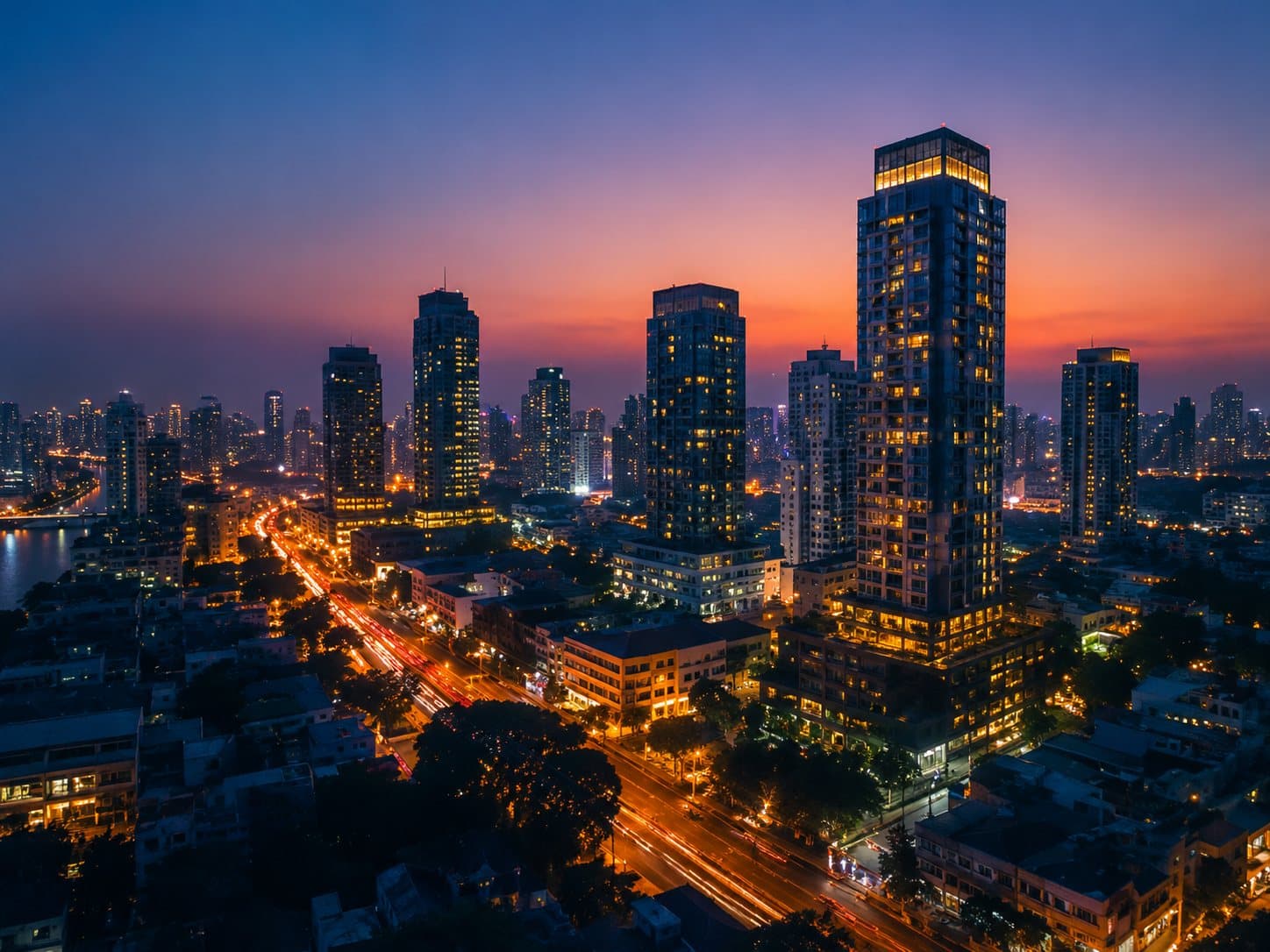 Bangkok condo towers lit up at dusk above a busy road, seen from above.